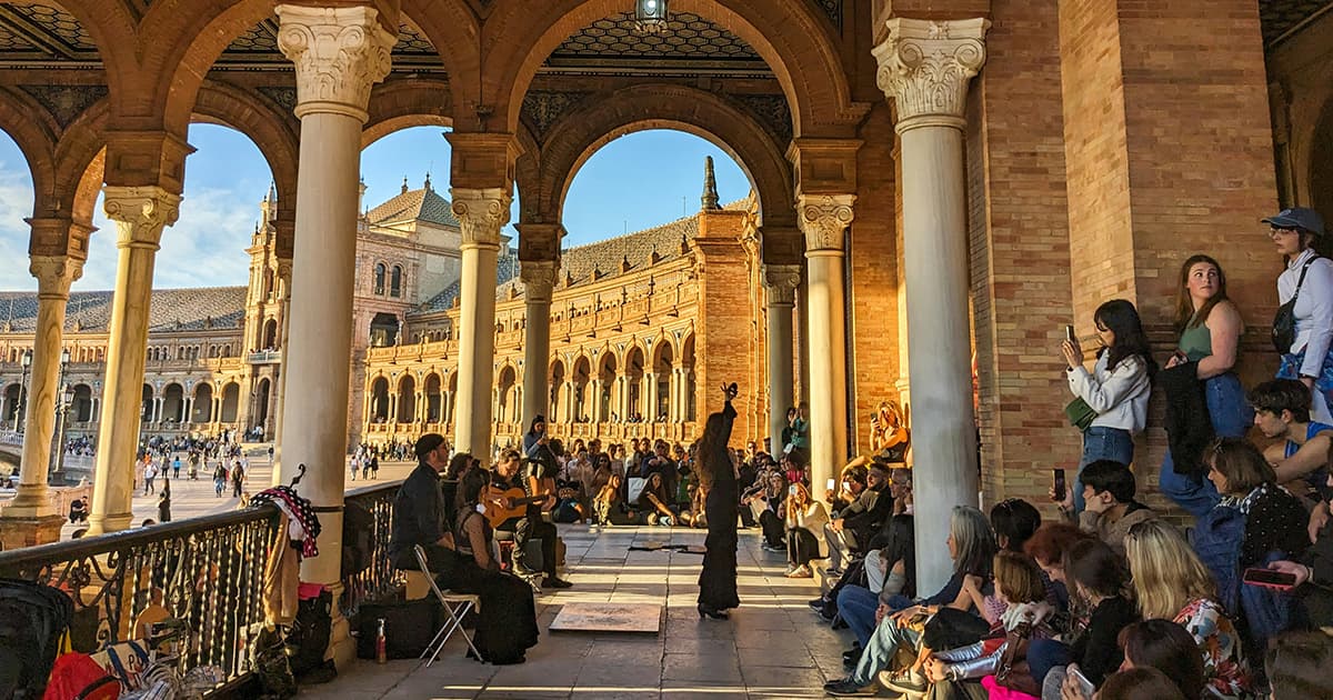 Flamenco performance under the arches at Plaza de España in Seville, Spain, with a crowd of spectators watching the dancers and musicians.