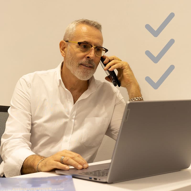 Chasseur-Immobilier-au-telephone-avec-ses-clients-1 Real estate advisor speaking on the phone while working on a laptop, coordinating a client’s search