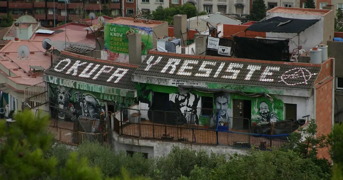 Occupied building in Spain with graffiti and banner reading 'Okupa y Resiste', symbolizing anti-eviction movement