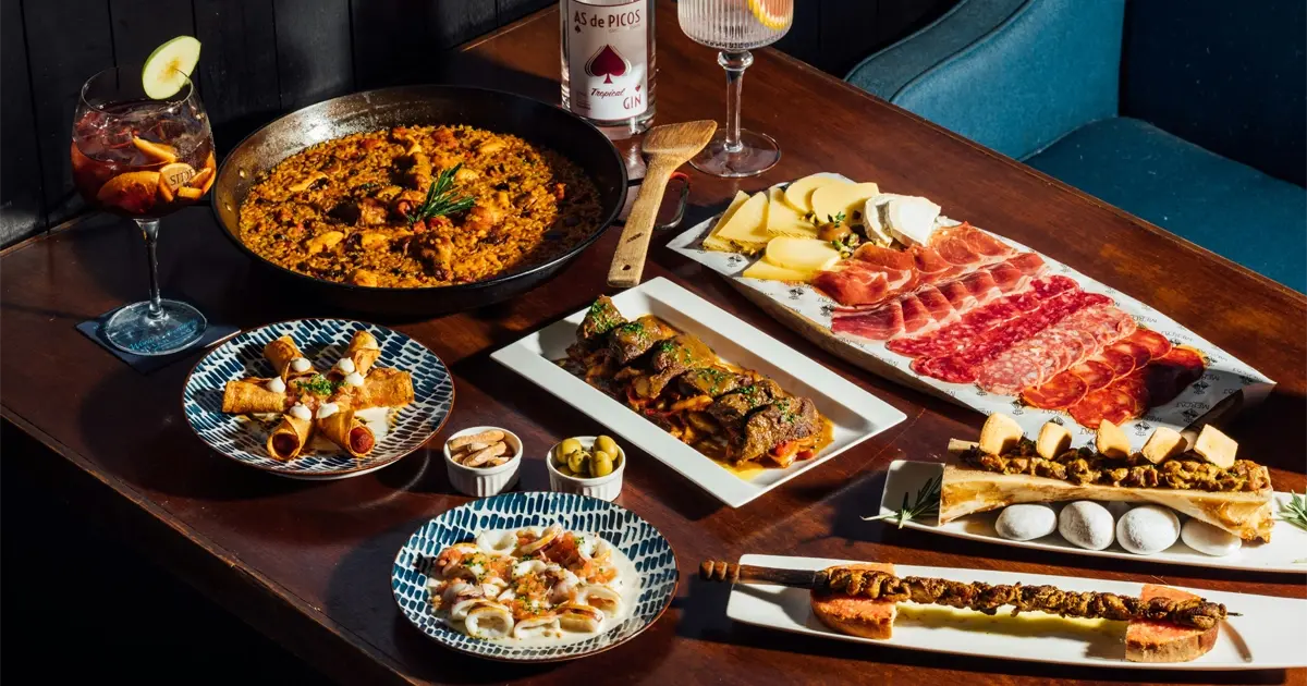 Table filled with Spanish specialties including paella, tapas, cold cuts and cheese, served with cocktails